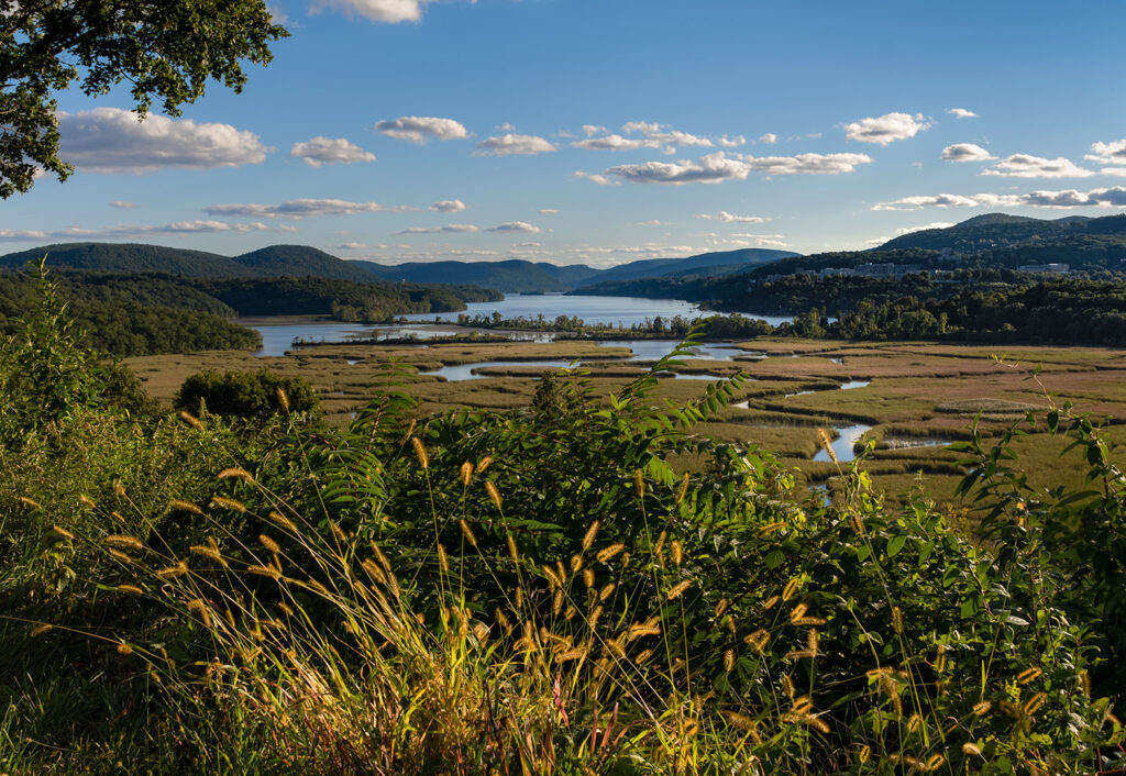 Discover Constitution Marsh Sanctuary: A Peaceful Hudson Valley Wetland - Hudson Valley Luxury Resorts Constitution Marsh Sanctuary with winding water channels, rolling hills, and the Hudson River in the background.