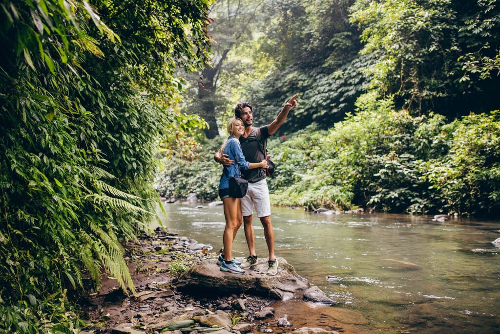 Couple Exploring Marlboro Mountain Trail: A Scenic Hudson Valley Escape - Hudson Valley Luxury Resorts A couple standing on a rock by a small stream, surrounded by dense green foliage, during a hike along Marlboro Mountain Trail in the Hudson Valley.