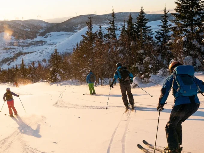 Skiers going down a snowy hill during sunset.